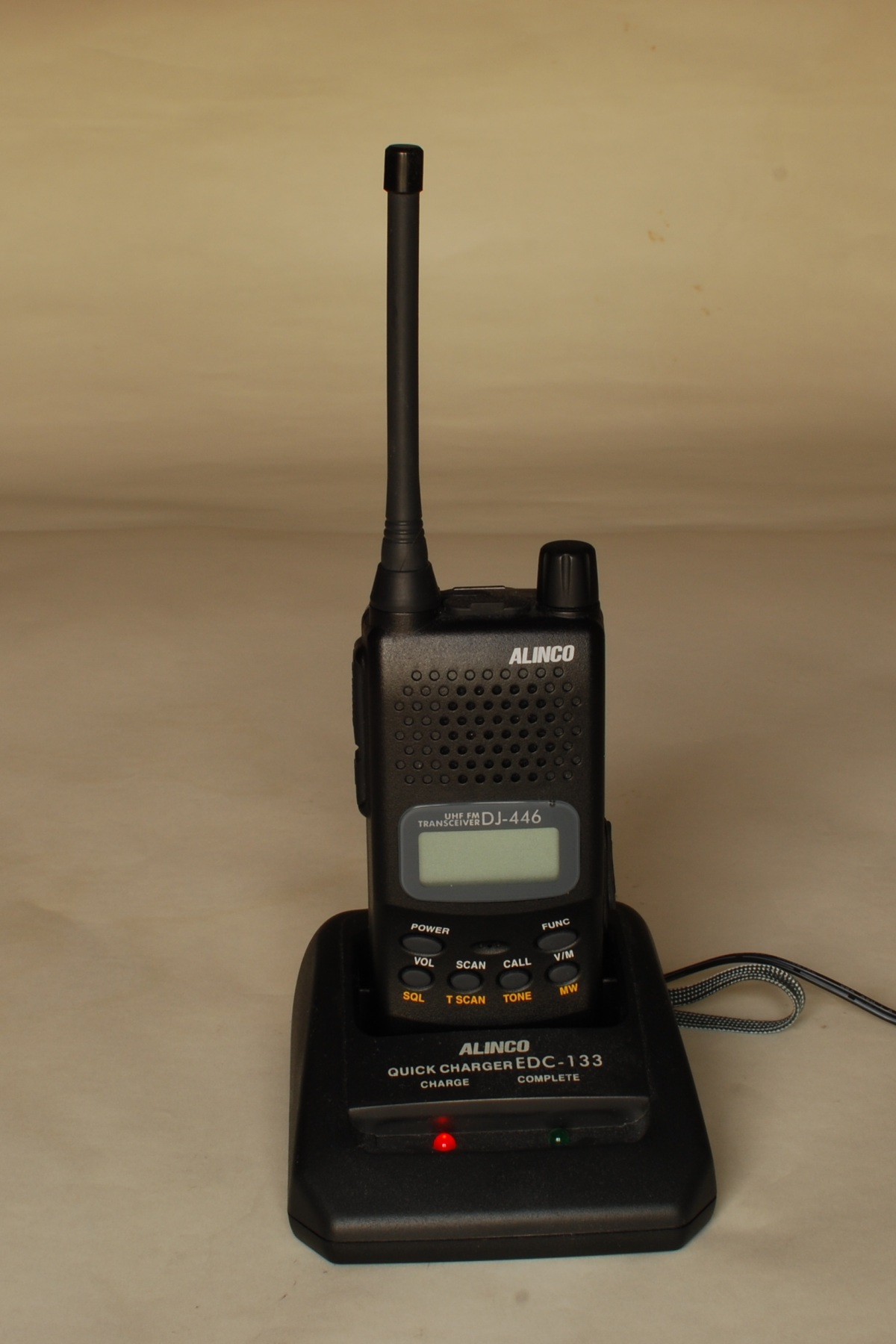 Alinco DJ-446 handheld two-way radio seated in a charging base.