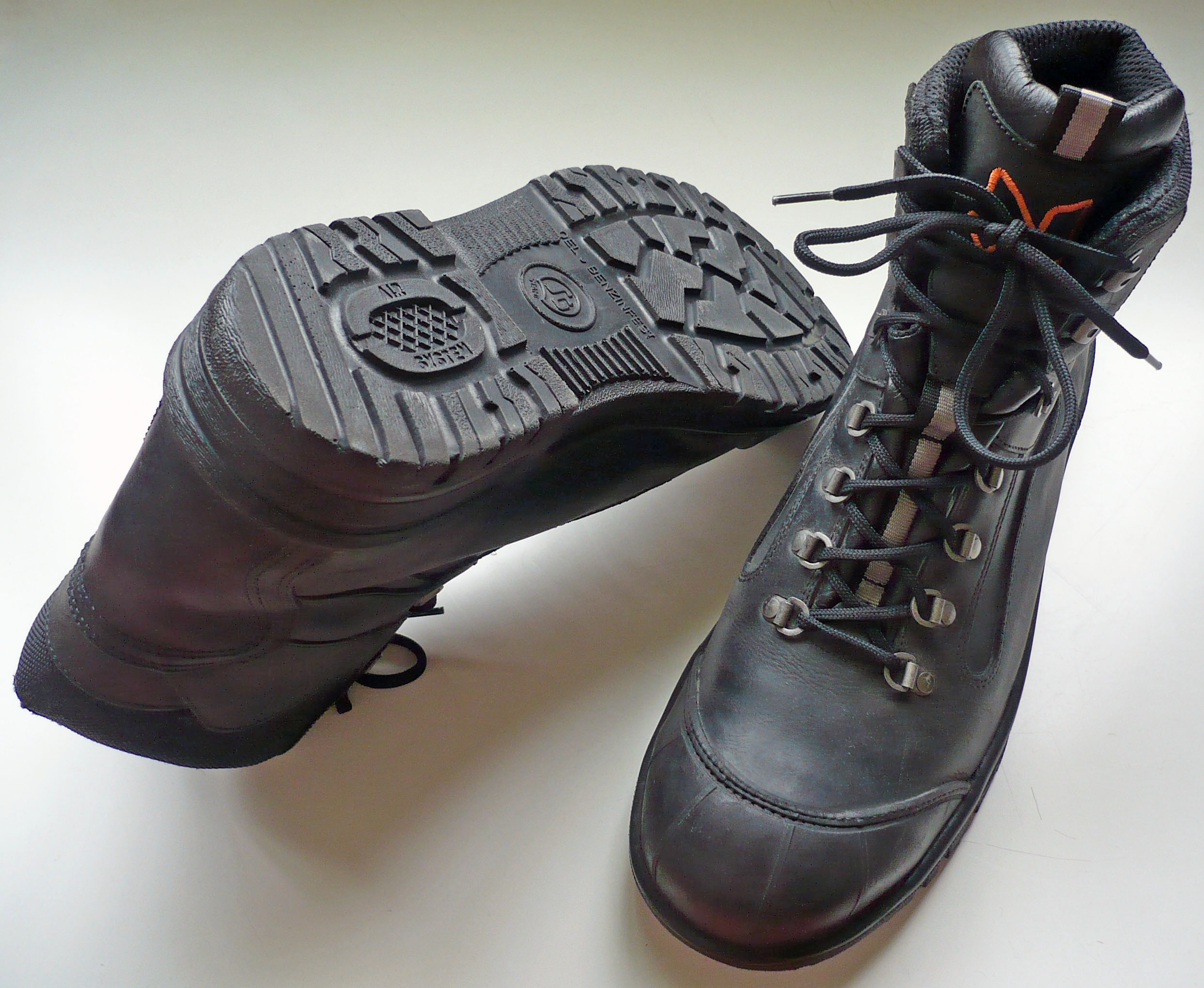 Two black lace-up safety boots, with one turned over to show its patterned outsole.