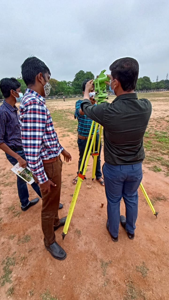 Four students gathered around a green theodolite mounted on a yellow tripod outdoors.